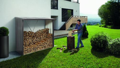 Man am Holzhacken im Garten vor einem dunkelgrauen Brennholzlager