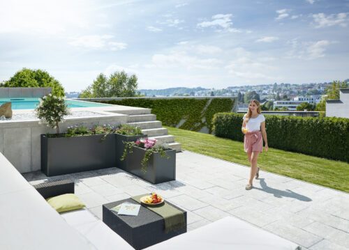 Das biohort DaVinci in dunkelgrau metallic auf einer grossen Terrasse mit Pool und Gartenlounge. Softub Schweiz