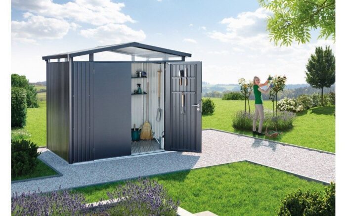 biohort Garden Shed Panorama. A big, metallic garden shed with pitched roof. The garden shed stands on a stony floor in a garden.