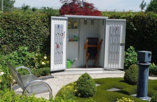 Metallschrank im Garten und offen stehenden Türen. Diverse Gartenutensilien sind im Geräteschrank verstaut und weggeräumt.