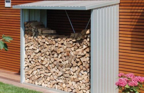 Biohort WoodStock - Holzlager in verschiedenen Farben und Grössen. Metallholzlager. Holz ist darin gestapelt. Rechts vom Holzlager stehen Blumen.