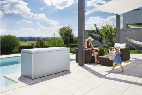 Terrasse mit Pool, Biohort Gartenbox in silber und Gartenlounge. Eine Frau mit Sonnenhut sitzt in der Gartenlounge.